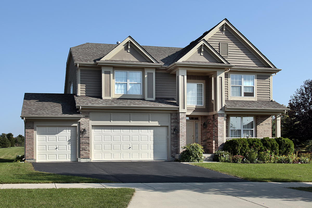 American style, brick residential home in suburbs with arched entrance, driveway and green gras.