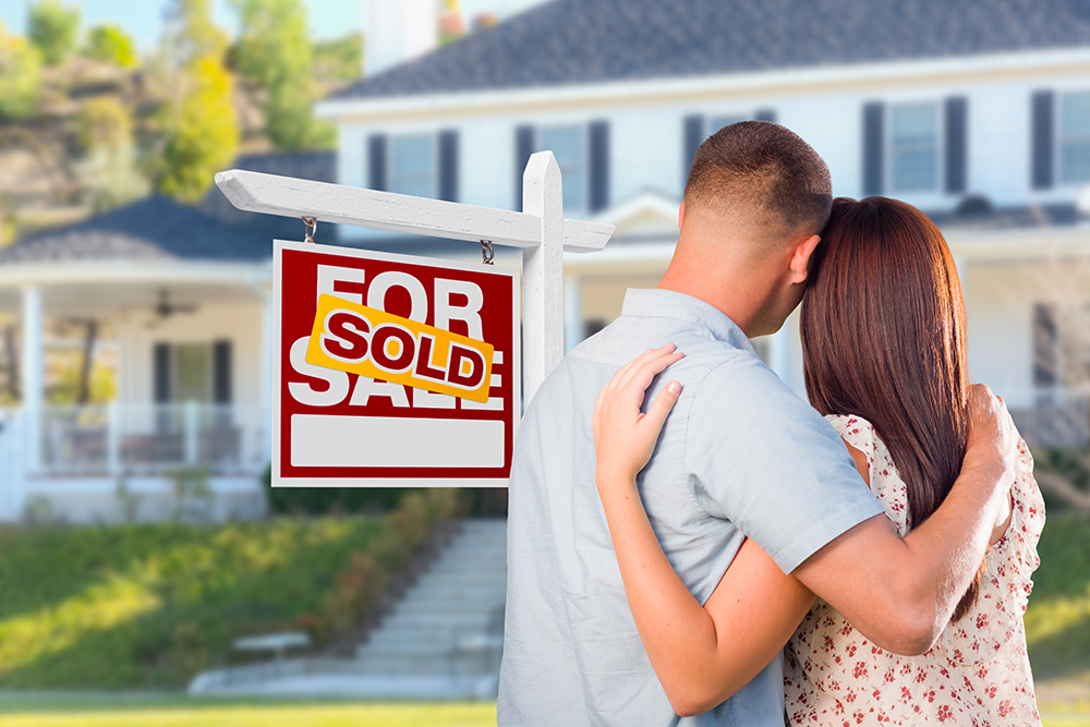 Couple Looking At House with Sold For Sale Real Estate Sign In Front.