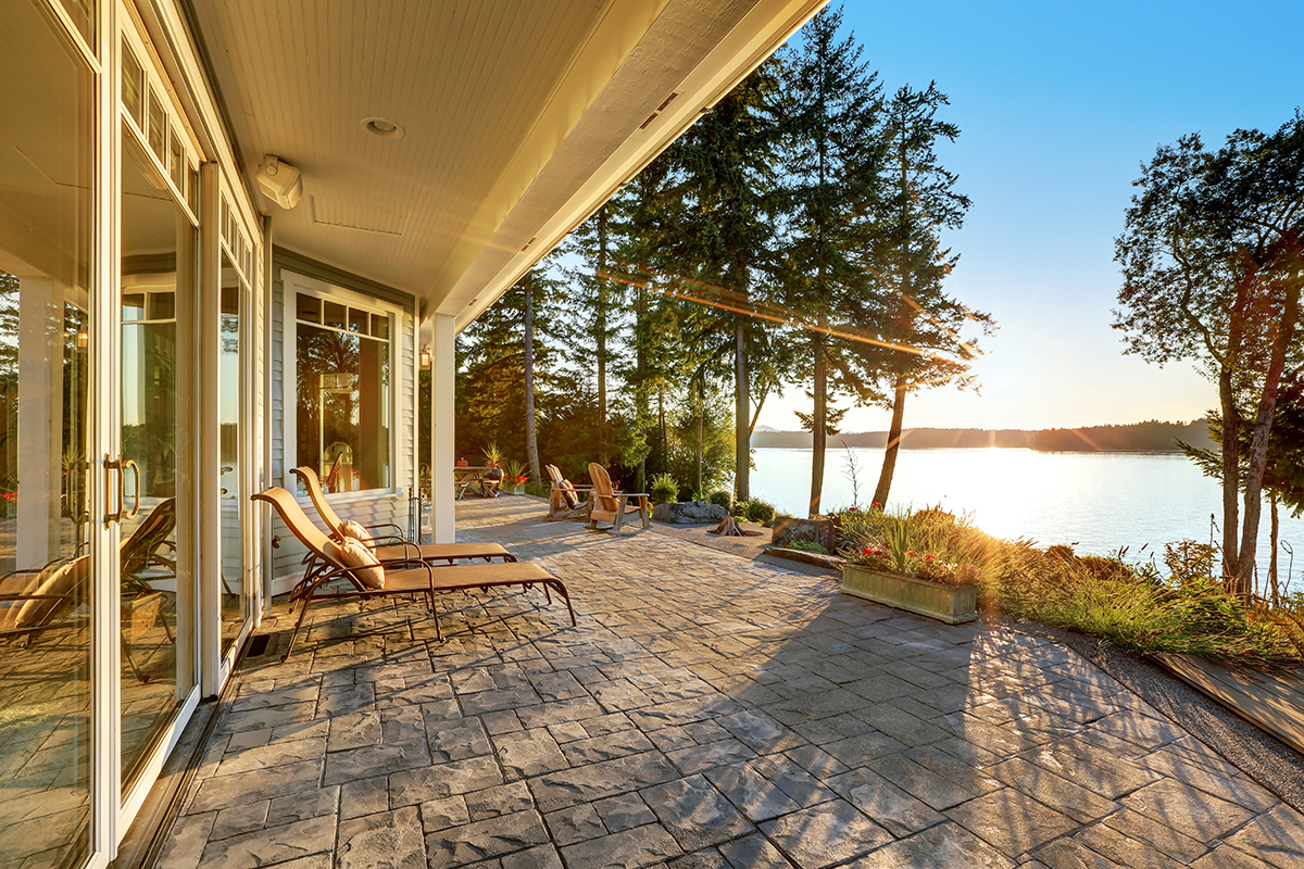 Large stone floor patio area of waterfront house with outdoor furniture, beautiful water view at sunset