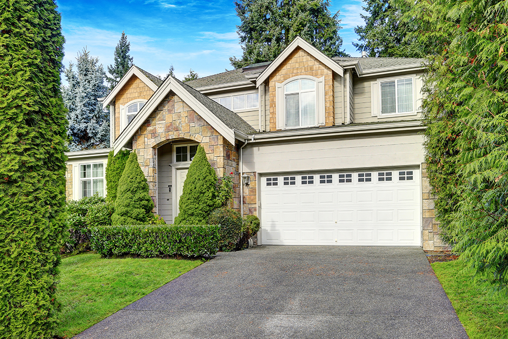 Craftsman-inspired house exterior with grey wood siding mixed with neutral stone accents and well manicured landscape design.