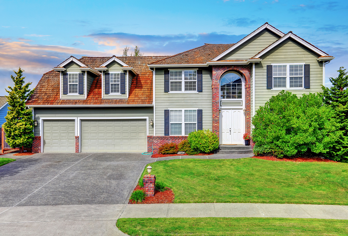 Luxury house exterior with red brick trim and arched entry. Double doors garage with concrete driveway.